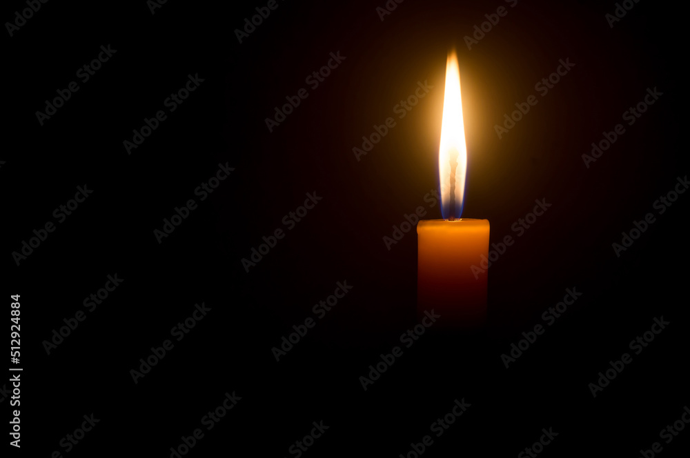 A single burning candle flame or light glowing on a yellow candle isolated on black or dark background on table in church for Christmas, funeral or memorial service A single burning candle flame or light glowing on a yellow candle isolated on black or dark background on table in church for Christmas, funeral or memorial service