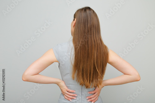 Woman in business dress standing back and keeps hands on hips, female portrait with long hair. Back view. Rear view.