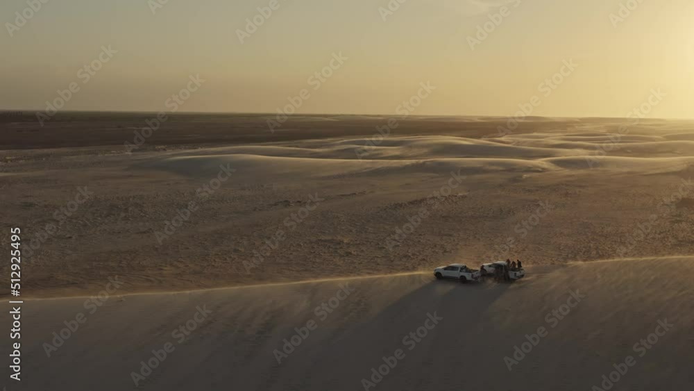 Epic view of offroad trucks on windy sand dune top in warm sunset glow; drone Epic view of offroad trucks on windy sand dune top in warm sunset glow; drone