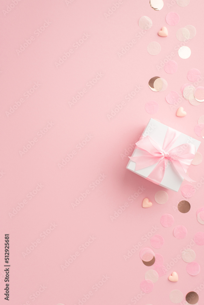 Gender party concept. Top view vertical photo of white giftbox with ribbon bow hearts and shiny confetti on isolated pastel pink background