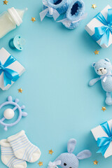 Baby concept. Top view vertical photo of gift boxes shoes socks pacifier teddy-bear teether bottle knitted bunny rattle toy gold stars on isolated pastel blue background with copyspace in the middle
