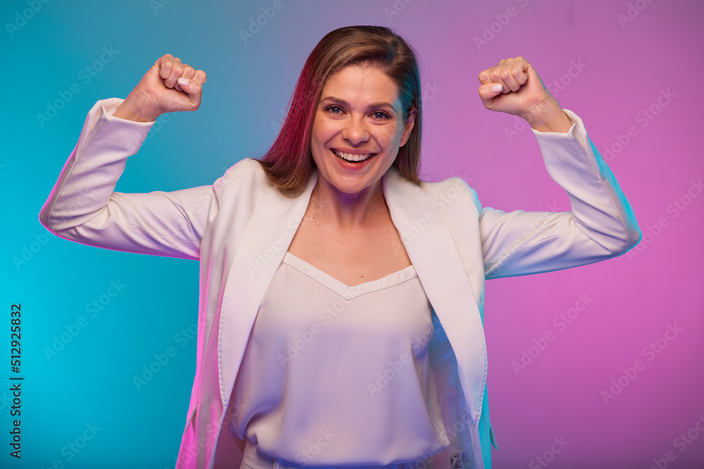 Fototapeta premium Smiling business woman bends his arms demonstrating muscles and female power, portrait with neon lights colors effect. Female model isolated on neon colored background wearing white suit.