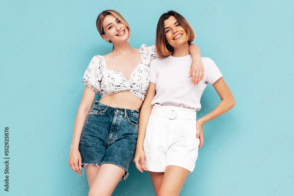 Two young beautiful smiling brunette hipster female in trendy summer shorts clothes. Sexy carefree women posing near blue wall. Positive models having fun. Cheerful and happy Two young beautiful smiling brunette hipster female in trendy summer shorts clothes. Sexy carefree women posing near blue wall. Positive models having fun. Cheerful and happy