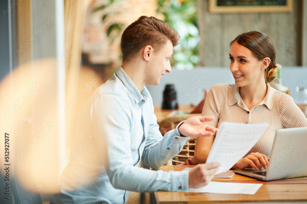 Positive young entrepreneurs in casual outfits sitting at table in coffee shop and discussing contract Positive young entrepreneurs in casual outfits sitting at table in coffee shop and discussing contract
