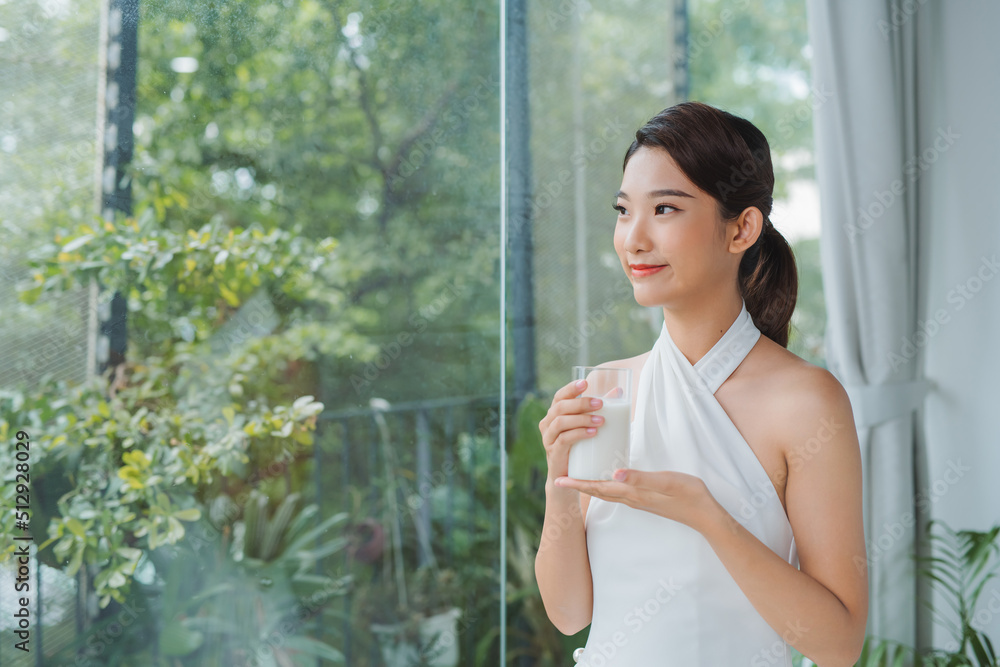 Asian lady drinking glass of milk while looking out the window Asian lady drinking glass of milk while looking out the window