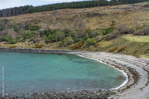 Tranquil cove with pristine clear blue waters and covered in pebble stones and coarse sand, located on the Isle of Raasay, a tiny secluded island off the west coast of Scotland, near Isle of Skye, UK