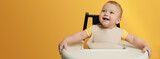 Cute little baby wearing bib in highchair on yellow background, space for text. Banner design