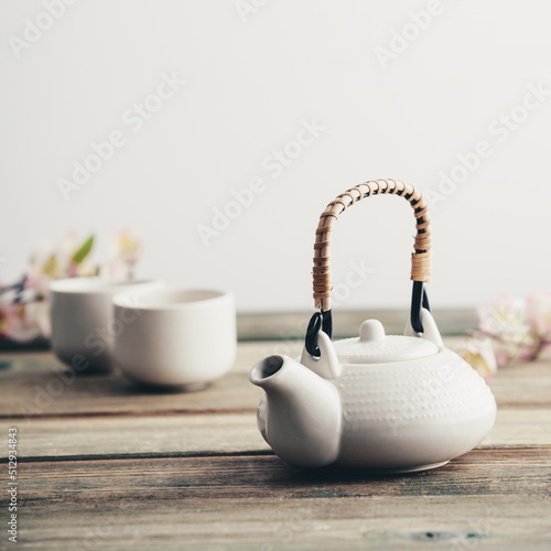 White teapot, cups, sakura flowers on wooden table against the white wall