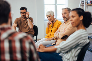 Serious-looking people carefully listening one male during the group therapy.