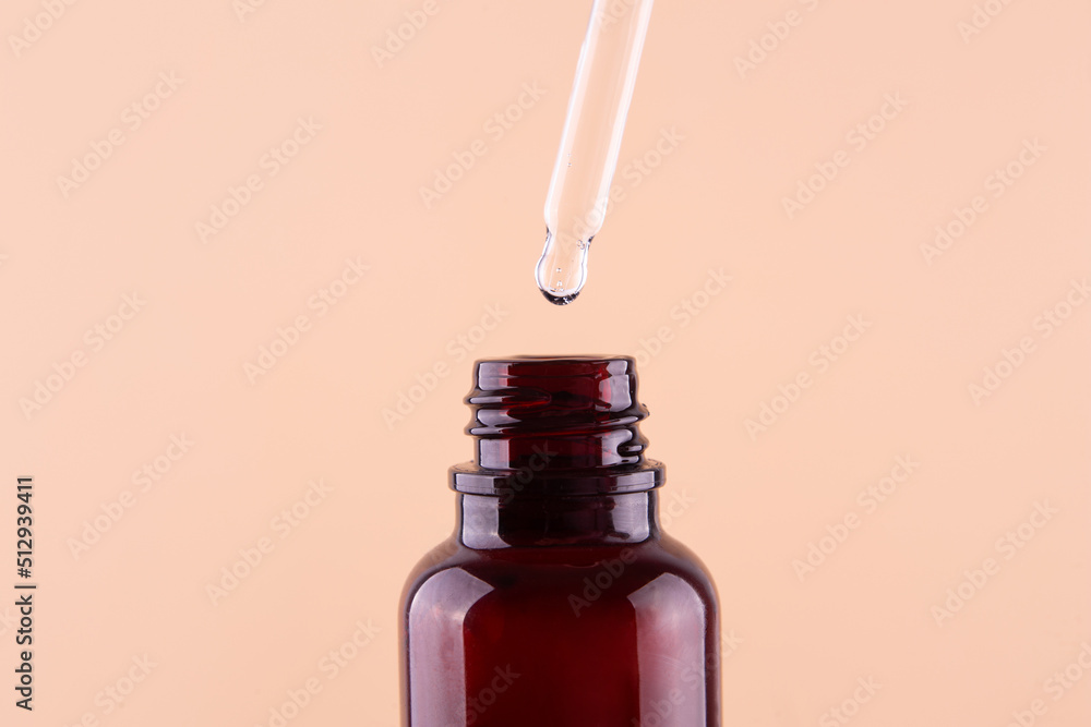 Oily drop dripping from pipette into cosmetic bottle close up, isolated on beige background. Oily drop dripping from pipette into cosmetic bottle close up, isolated on beige background.