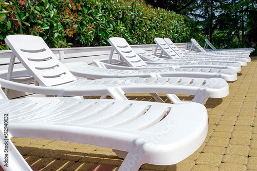 Many empty white loungers in row in luxury tropical resort hotel. Perspective, along green bushes. Summer holidays and vacation, travel and tourism concept. photo