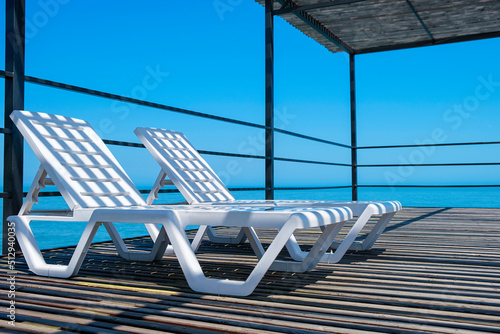 Two empty white loungers in row in luxury tropical resort hotel. Sea view from high pier. Summer holidays and vacation, travel and tourism concept photo