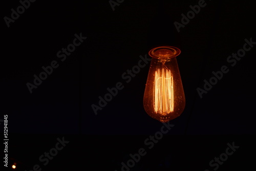 Classic lighting bulb in orange warm light over dark background.
