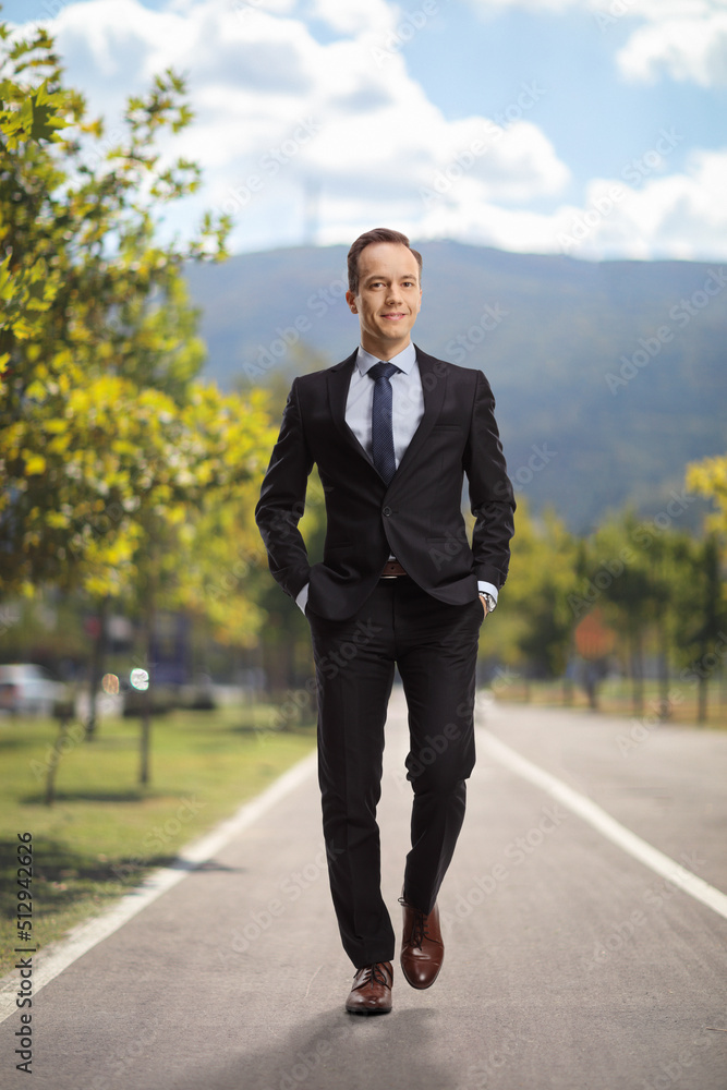 Full length portrait of a businessman walking towards camera with hands in pockets outdoors on a pedestrian lane Full length portrait of a businessman walking towards camera with hands in pockets outdoors on a pedestrian lane