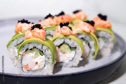 Closeup sliced rolls with shrimp in avocado, with salmon and black caviar on a plate, selective focus
