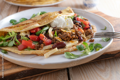 Ground beef dish with a fresh pancake or crepe filled with kidney beans, vegetables, cheese and topped with sour cream photo