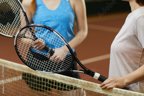 Close-up of unrecognizable female tennis players standing at net and holding personal racquets while discussing game © Mediaphotos