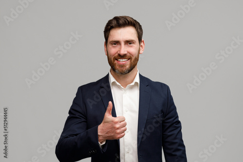 Portrait of smiling businessman riding his thumb up over grey studio background