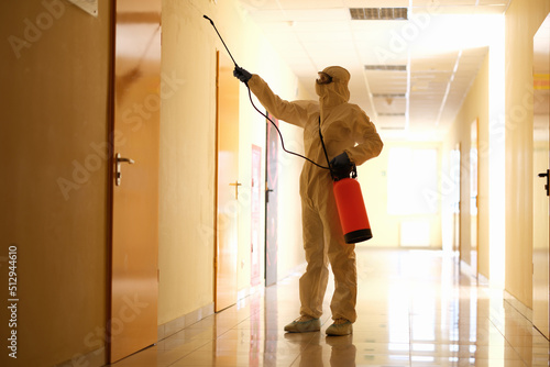 Person wearing white chemical protection suit holding spray bottle with disinfectant chemicals