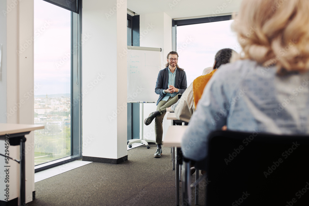 A young teacher is sitting in a classroom with group of multicultural senior students and teaching a lesson about marketing. A young teacher is sitting in a classroom with group of multicultural senior students and teaching a lesson about marketing.