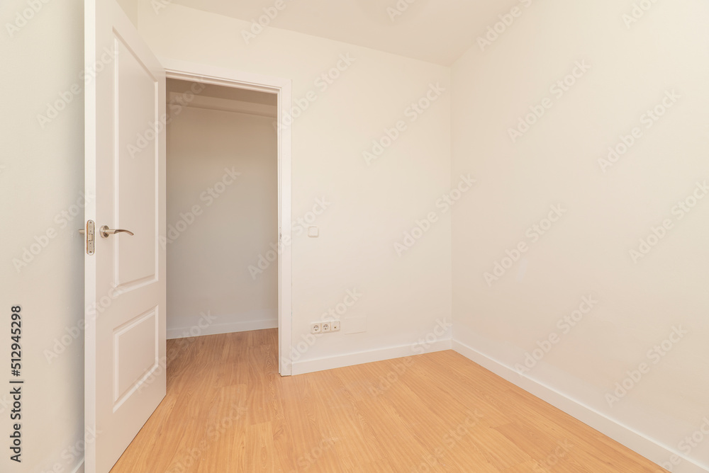 Empty room with light oak parquet flooring, plain white painted walls and white lacquered wooden door