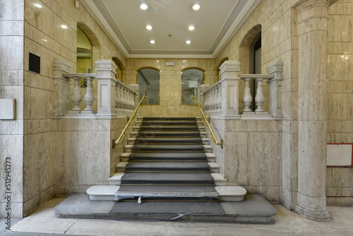 Stairs with steps and marble balustrade on the ground floor of a mansion with worn carpets
