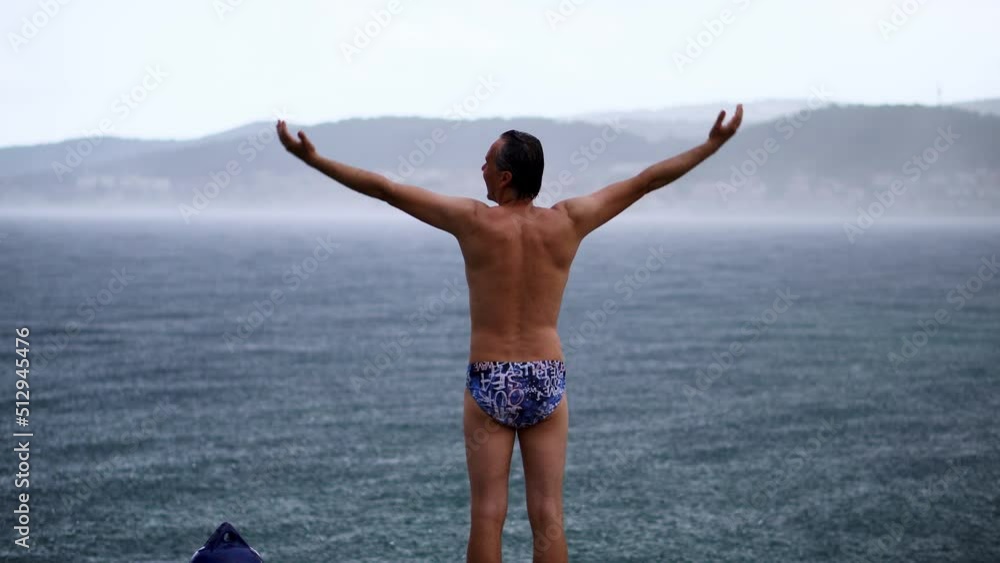 Back View Of A Man In Swimsuit Standing With Arms Outstretched At The Beach. full shot Back View Of A Man In Swimsuit Standing With Arms Outstretched At The Beach. full shot