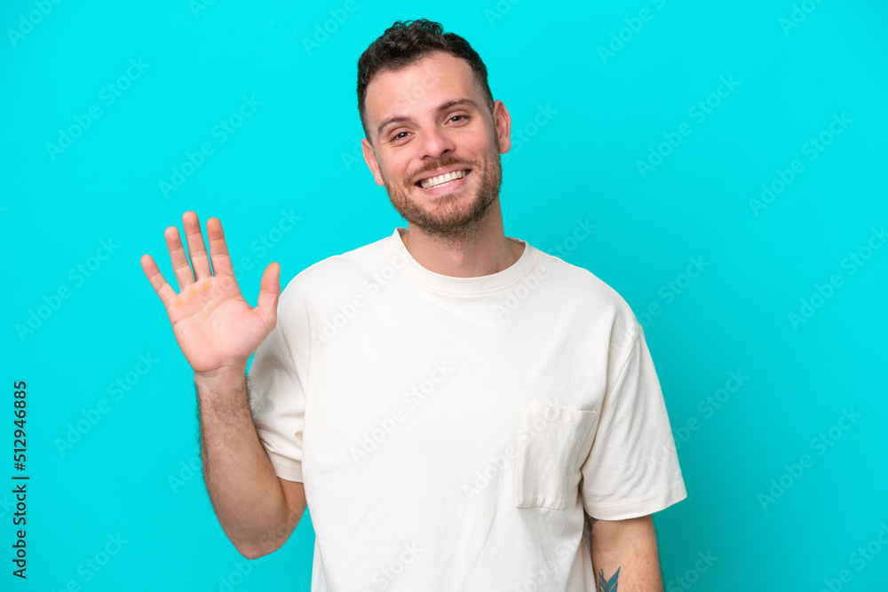 Young Brazilian man isolated on blue background saluting with hand with happy expression Young Brazilian man isolated on blue background saluting with hand with happy expression