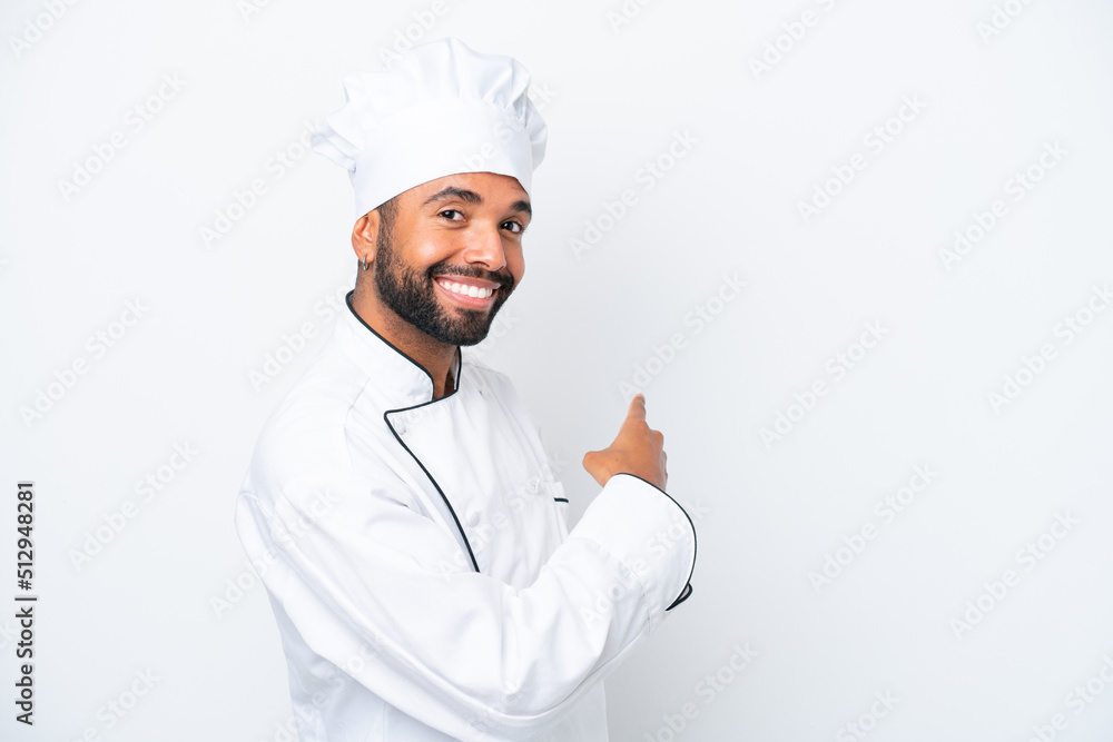 Young Brazilian chef man isolated on white background pointing back