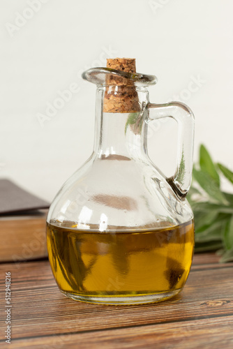 Fotografie Pure olive oil in a glass jar, a closed Bible Book, and a green olive branch on a wooden table with white background