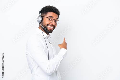 Telemarketer Brazilian man working with a headset isolated on white background pointing back