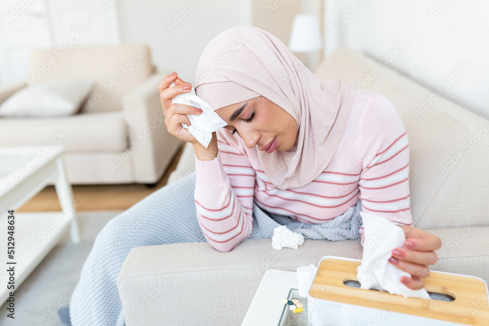 Fototapeta premium Sick day at home. Young Arabic woman has runny and common cold. Cough. Closeup Of Beautiful Young Woman with hijab Caught Cold Or Flu Illness.
