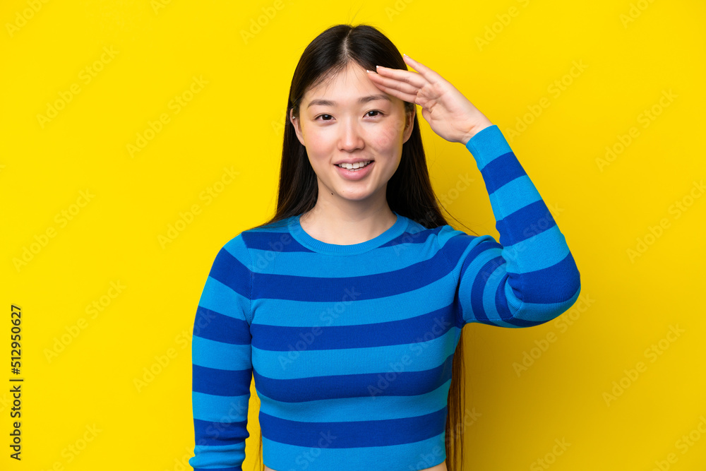 Young Chinese woman isolated on yellow background saluting with hand with happy expression Young Chinese woman isolated on yellow background saluting with hand with happy expression