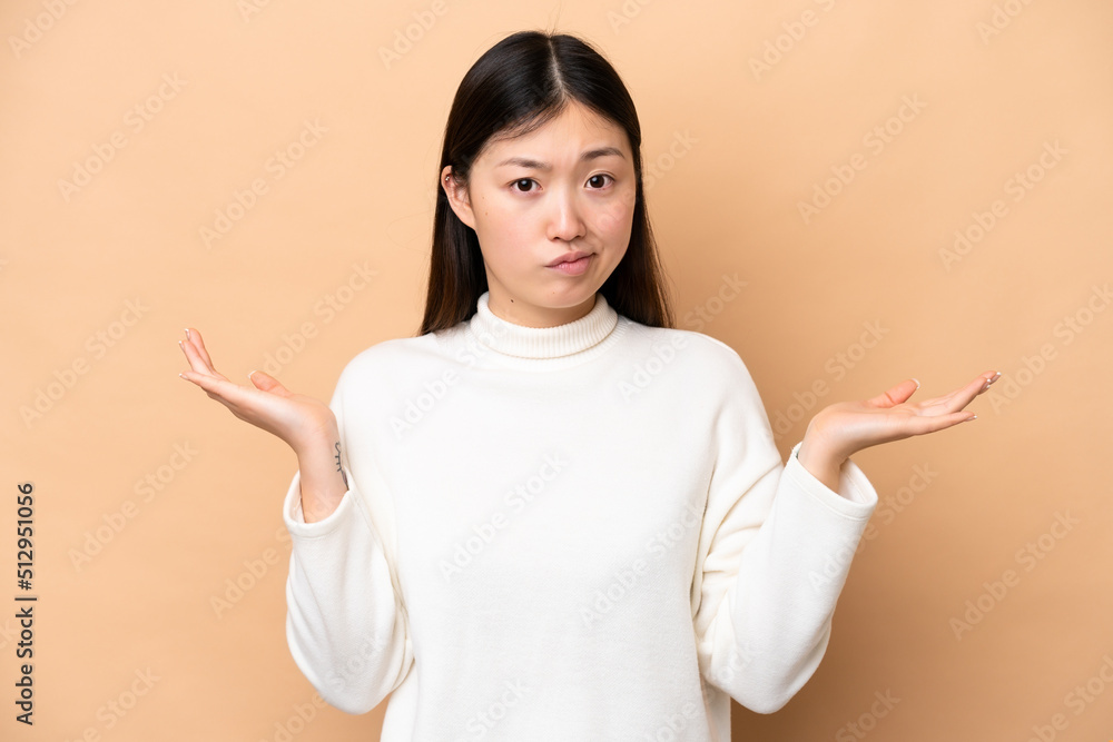 Young Chinese woman isolated on beige background having doubts while raising hands Young Chinese woman isolated on beige background having doubts while raising hands