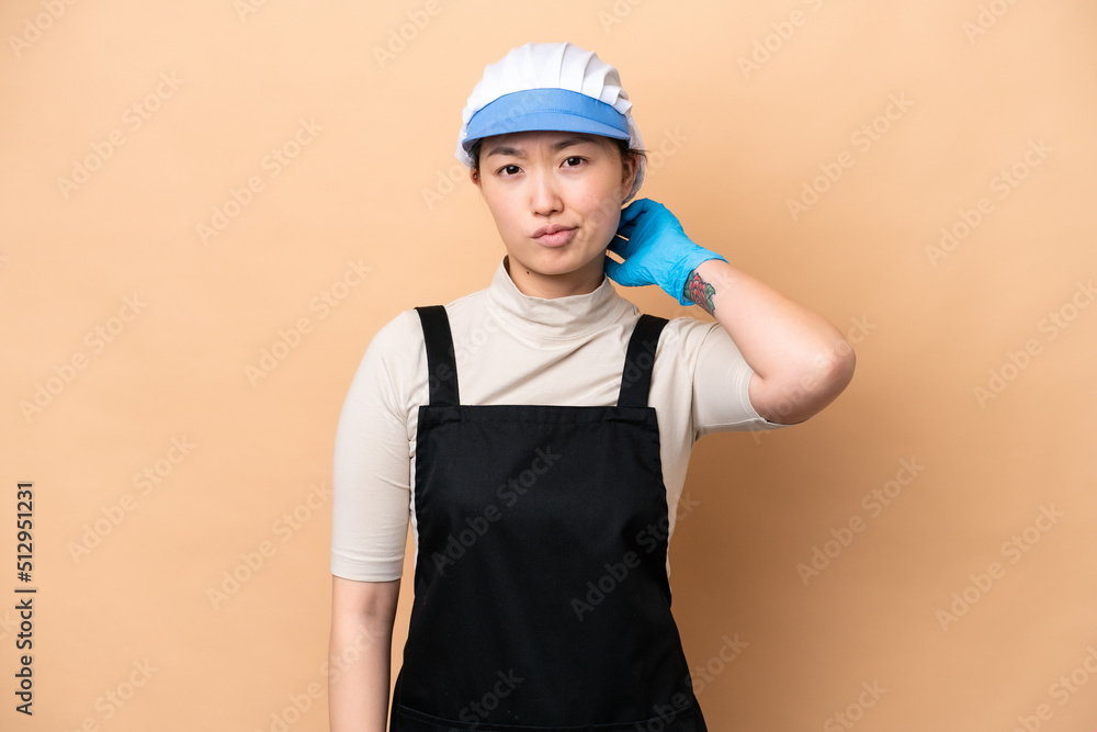 Young Chinese Fishmonger woman wearing an apron and holding a raw fish isolated on pink background having doubts Young Chinese Fishmonger woman wearing an apron and holding a raw fish isolated on pink background having doubts