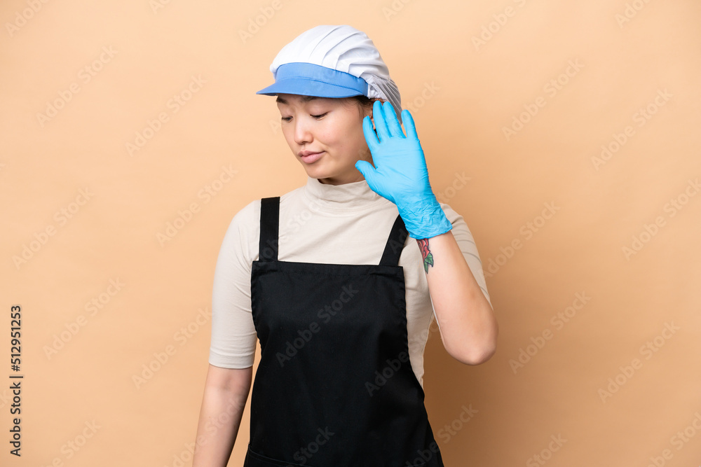 Young Chinese Fishmonger woman wearing an apron and holding a raw fish isolated on pink background making stop gesture and disappointed