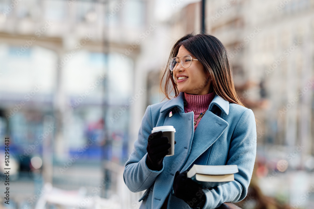 A happy multiracial young woman is standing outside and holding coffee and books she wants to read. A happy multiracial young woman is standing outside and holding coffee and books she wants to read.
