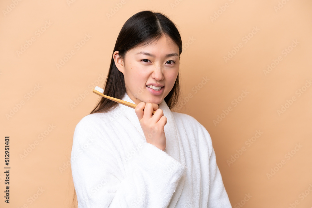 Young Chinese woman isolated on beige background with a toothbrush and happy expression Young Chinese woman isolated on beige background with a toothbrush and happy expression