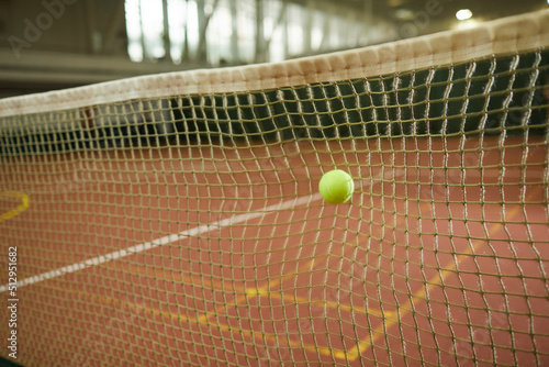 Close-up of green tennis ball hitting to net considered as out on indoor court, background of tennis game