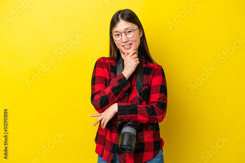 Young photographer Chinese woman isolated on yellow background with glasses and smiling