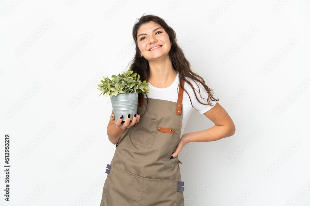Young Russian gardener girl holding a plant isolated posing with arms at hip and smiling Young Russian gardener girl holding a plant isolated posing with arms at hip and smiling