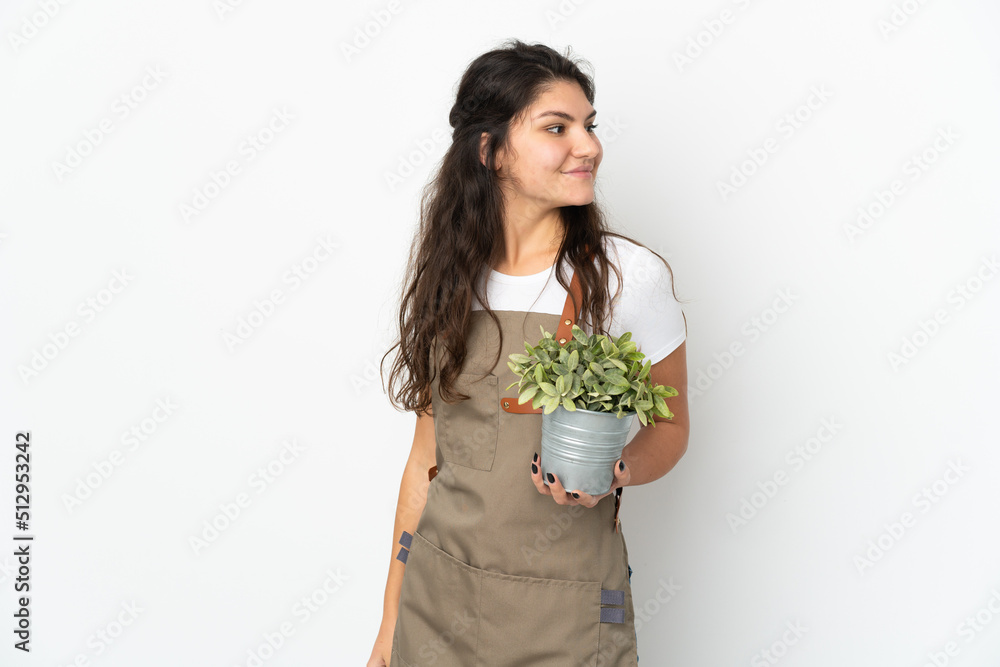 Young Russian gardener girl holding a plant isolated looking to the side and smiling Young Russian gardener girl holding a plant isolated looking to the side and smiling