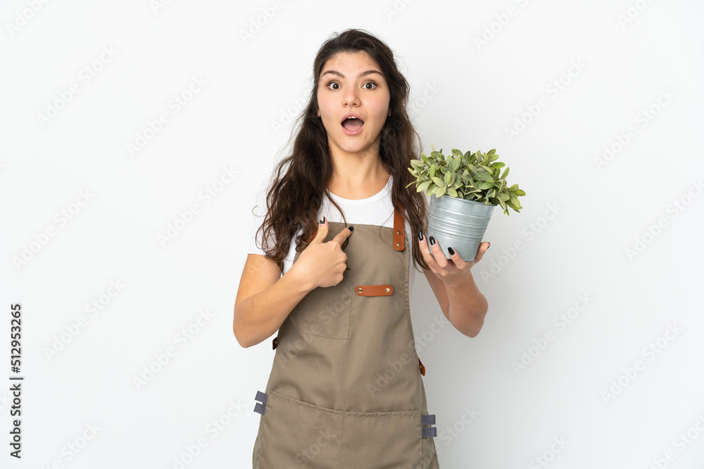 Young Russian gardener girl holding a plant isolated with surprise facial expression Young Russian gardener girl holding a plant isolated with surprise facial expression