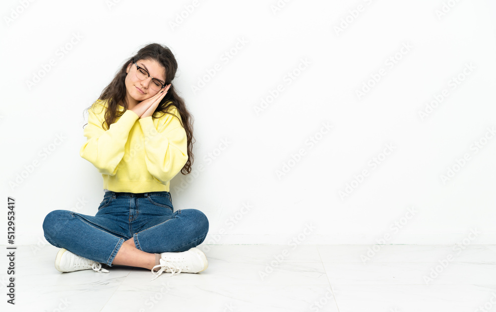 Teenager Russian girl sitting on the floor making sleep gesture in dorable expression Teenager Russian girl sitting on the floor making sleep gesture in dorable expression