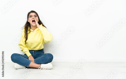 Teenager Russian girl sitting on the floor shouting with mouth wide open