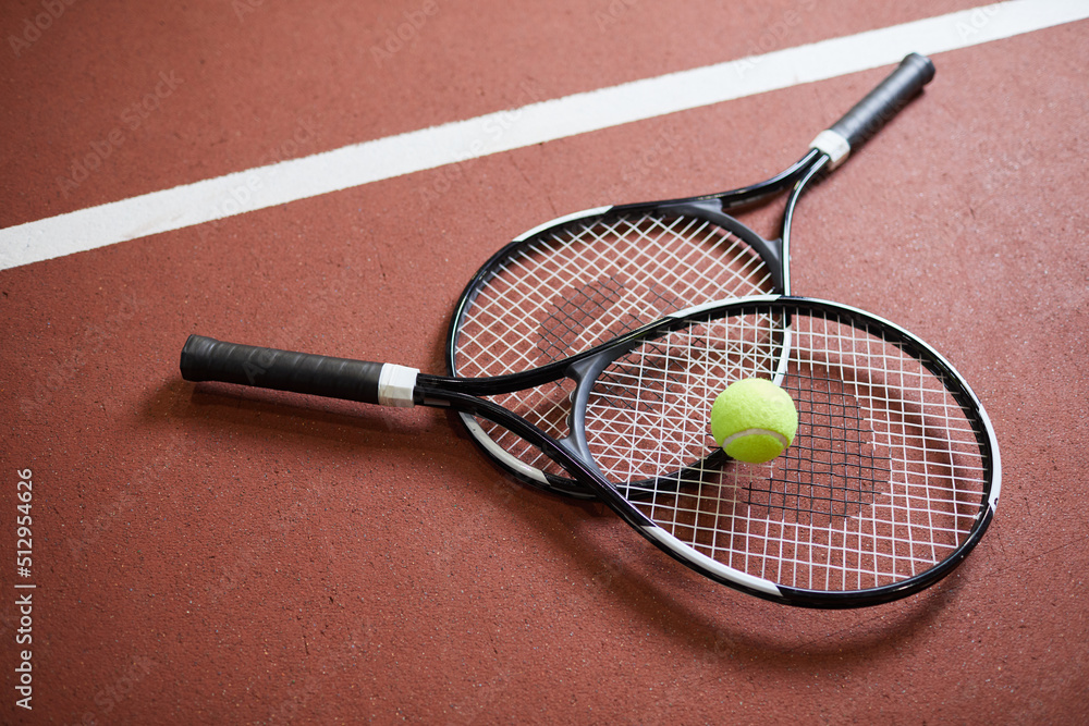 Close-up of black modern rackets with light green ball lying on tennis court floor, sport and hobby concept