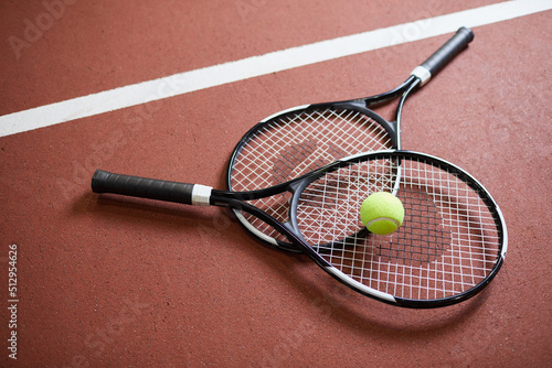Close-up of black modern rackets with light green ball lying on tennis court floor, sport and hobby concept © Mediaphotos