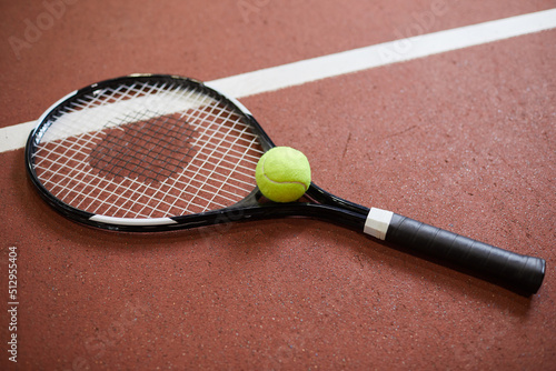 Close-up of tennis racquet and green ball placed on red floor of tennis court, copy space © Mediaphotos