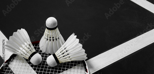 White cream badminton shuttlecock  and rackets on dark floor of the indoor badminton court, soft and selective focus on shuttlecock, concept for badminton sports around the world.
