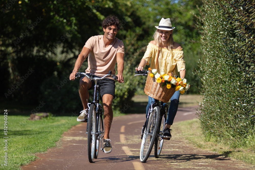 happy young couple riding bicycles along road in summer